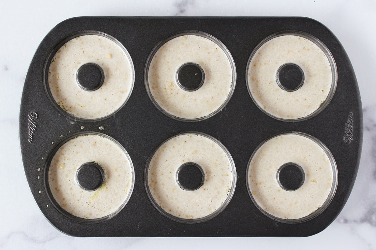 Donut batter in six wells in a metal donut pan.