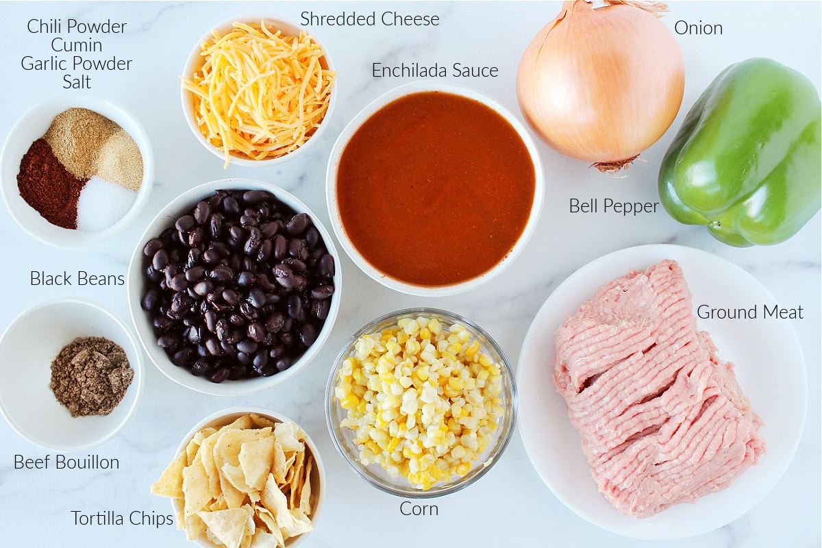 Labeled ingredients for ground beef enchilada casserole on a white marble countertop.