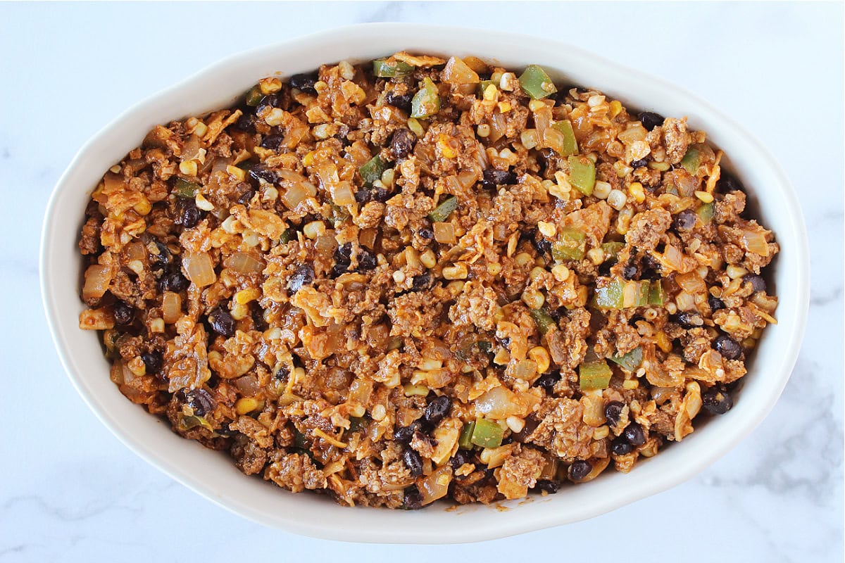 Ground meat, veggies and black beans in an enchilada sauce in an oval baking dish.