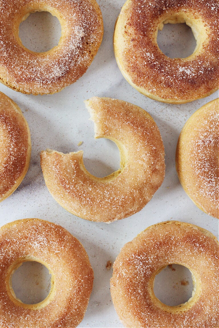 A bite taken out of the middle cinnamon sugar donut surrounded by golden brown donuts.