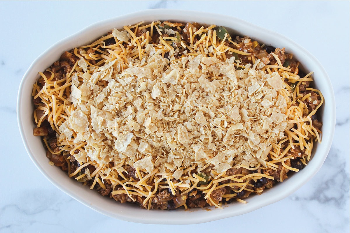 Crushed tortilla chips on top of shredded cheese on an enchilada casserole.
