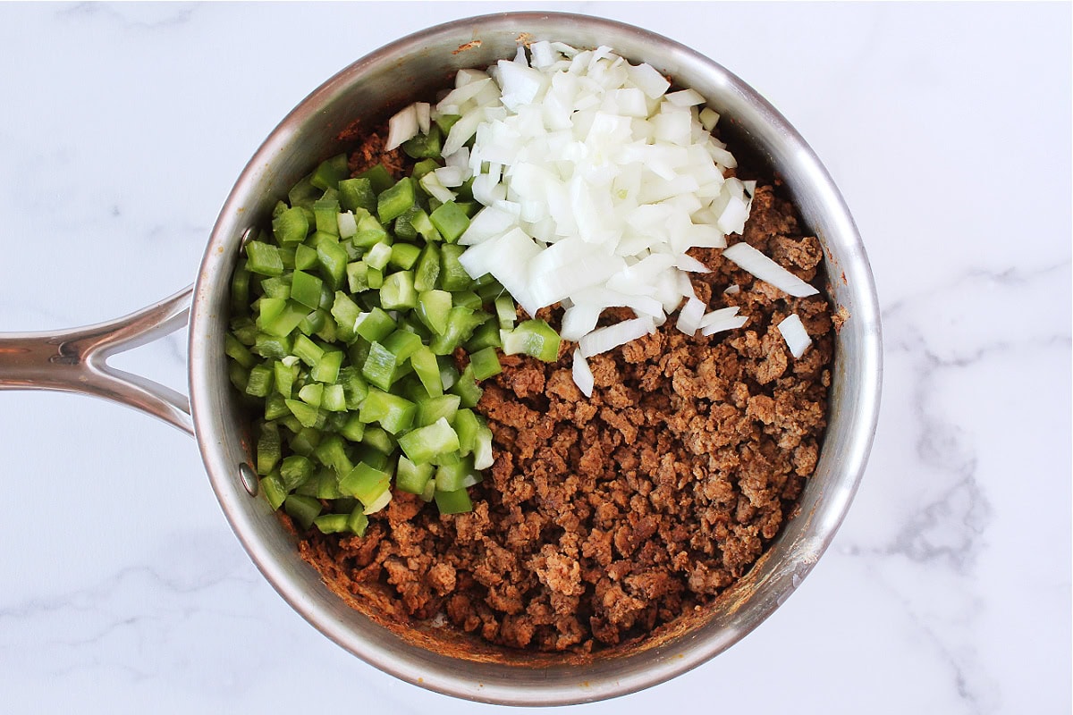 Browned ground meat with diced green pepper and onion in a saute pan.