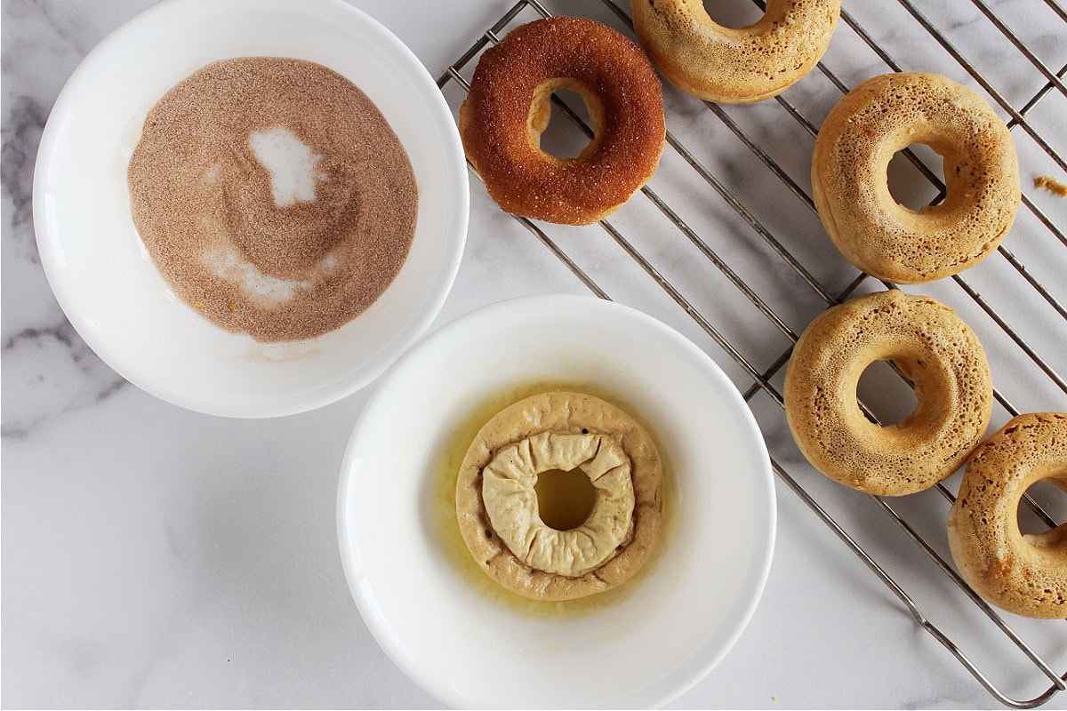 A baked donut dipped in melted butter in a bowl.