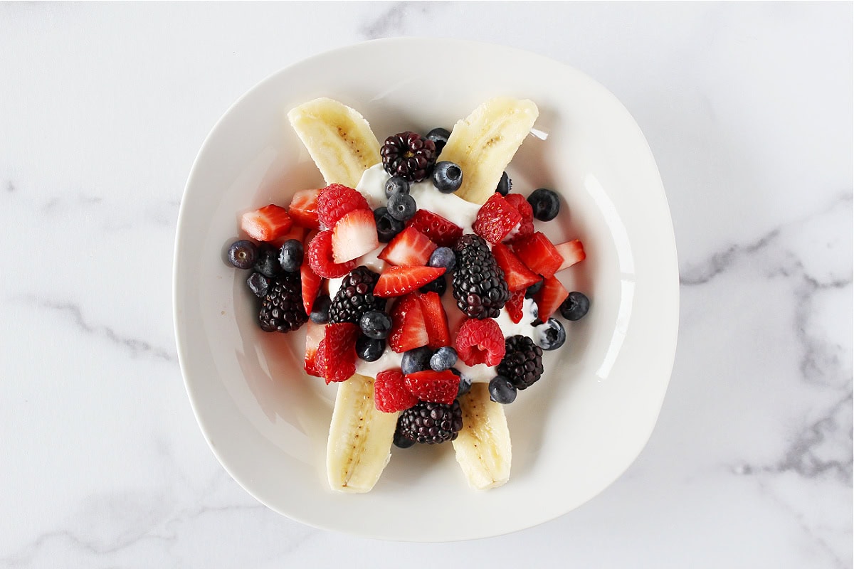 Fresh berries and plain Greek yogurt on two halves of a peeled banana.