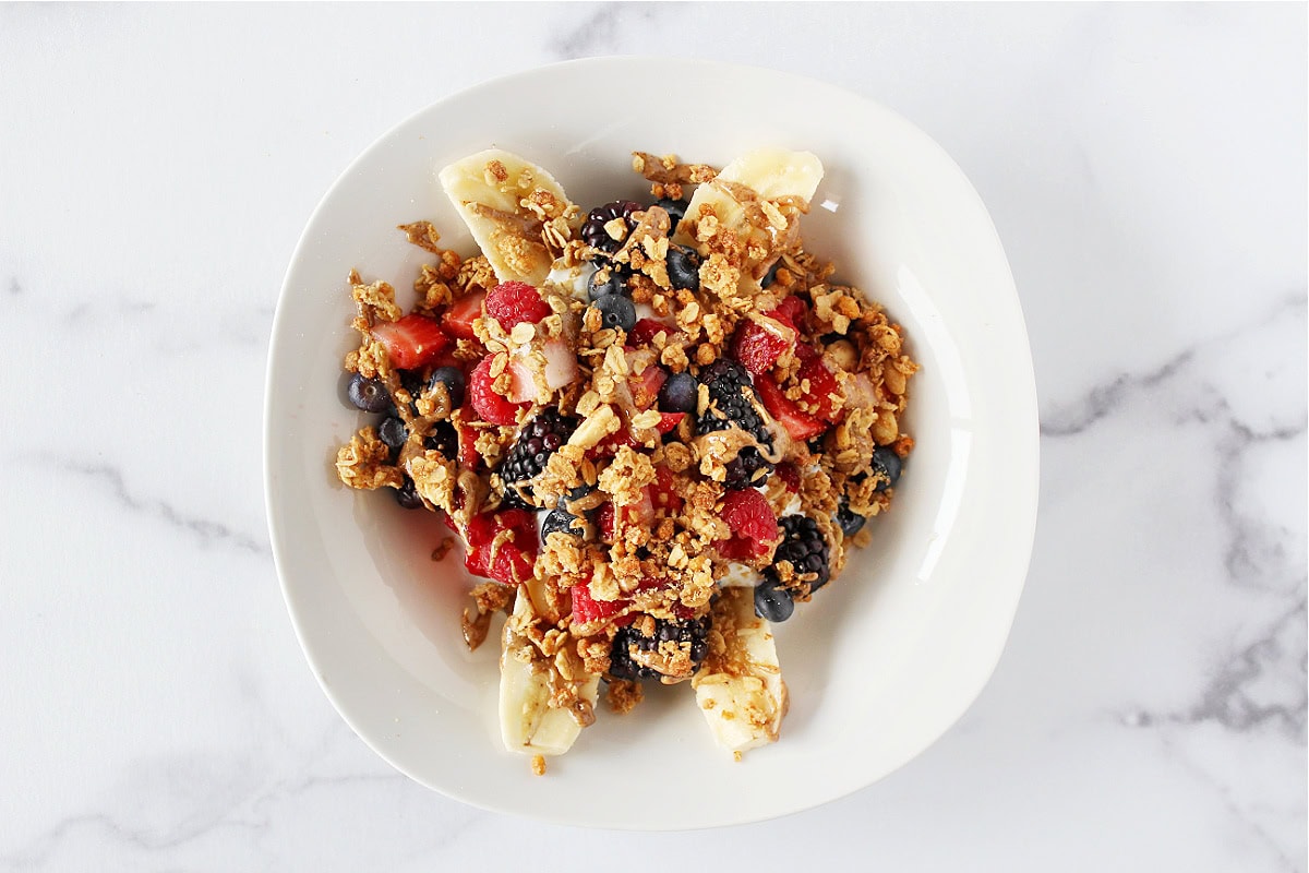 A breakfast banana split with granola, fresh berries, and nut butter on a plate.