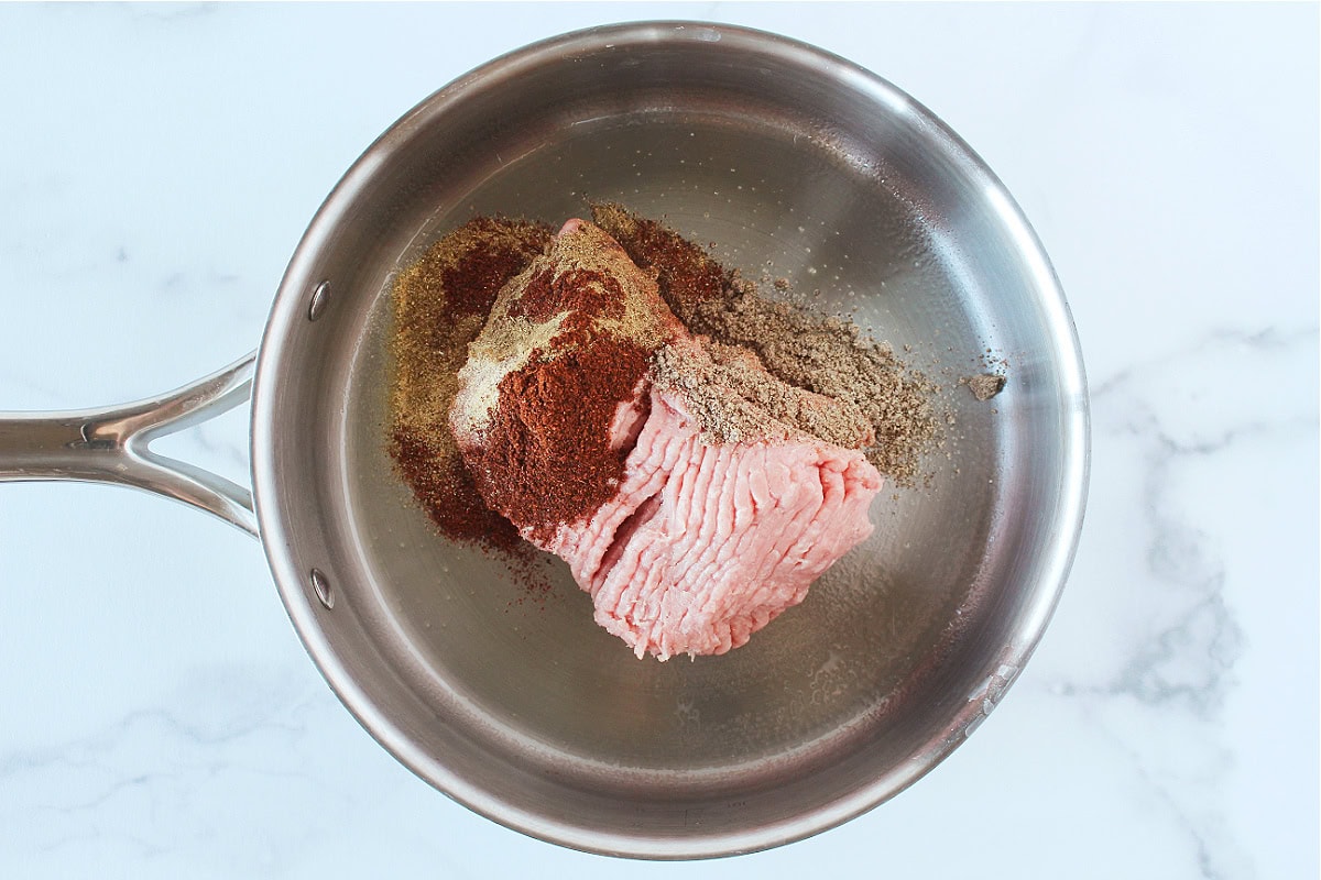 Raw ground meat with cumin and chili powder in a saute pan.