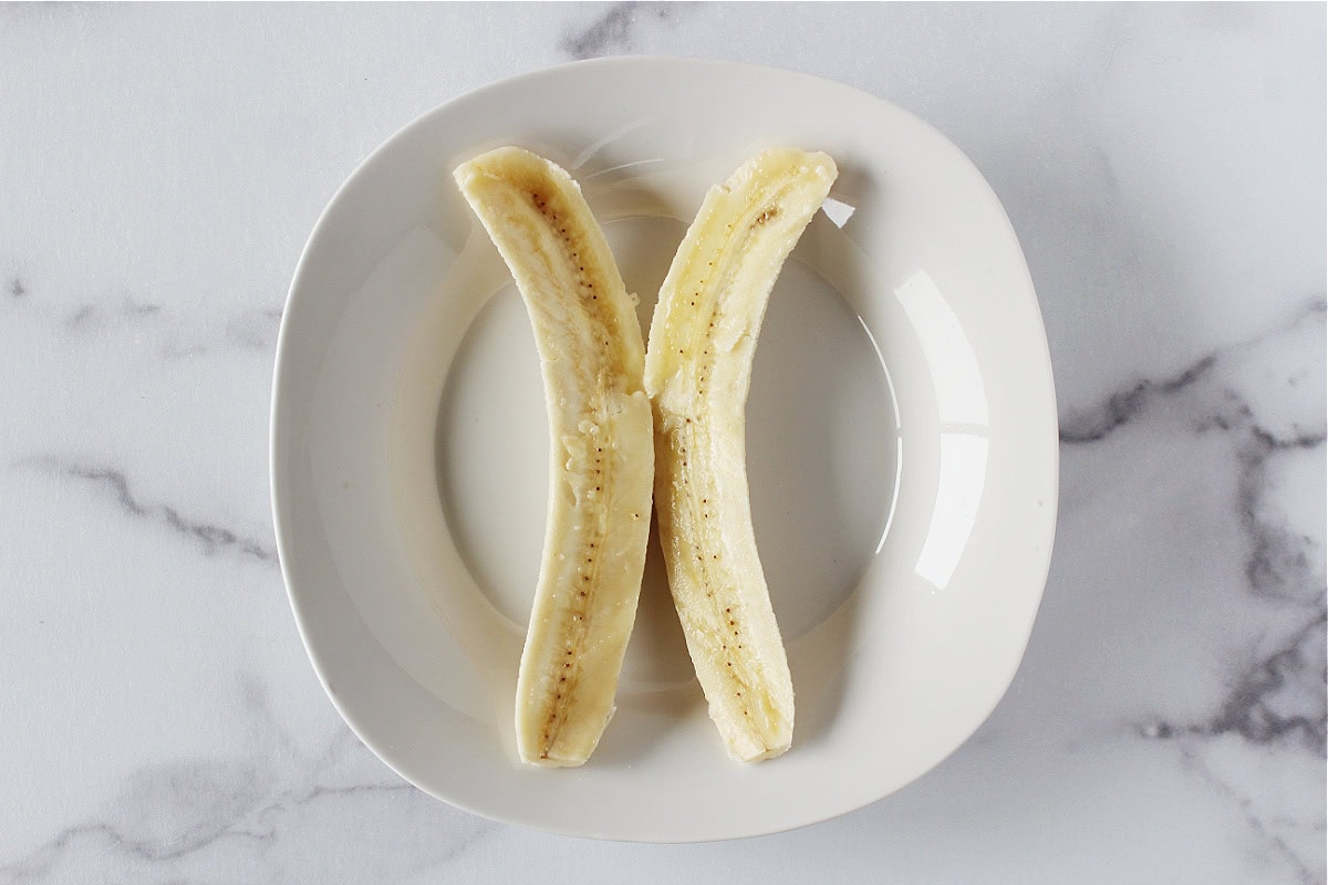 A peeled banana cut in half lengthwise on a white plate.