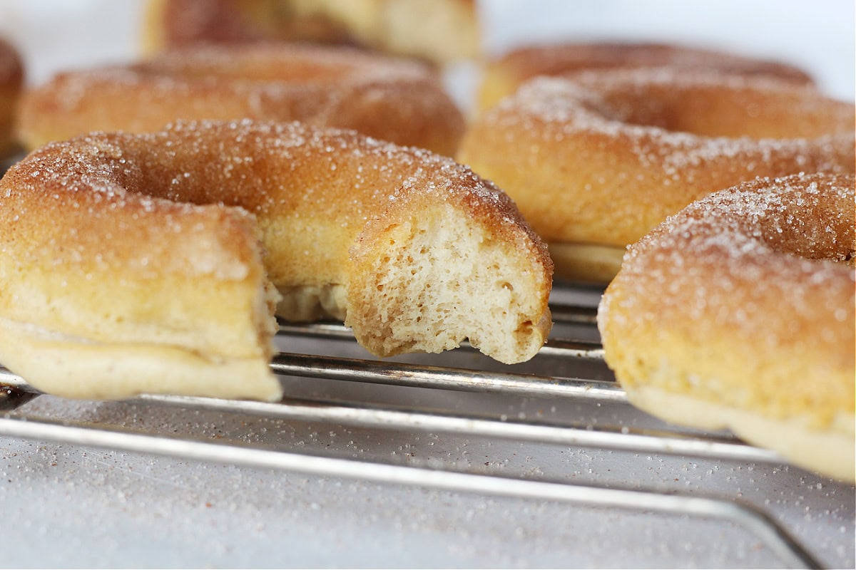 A bite taken out of a cinnamon sugar donut on a cooling rack.
