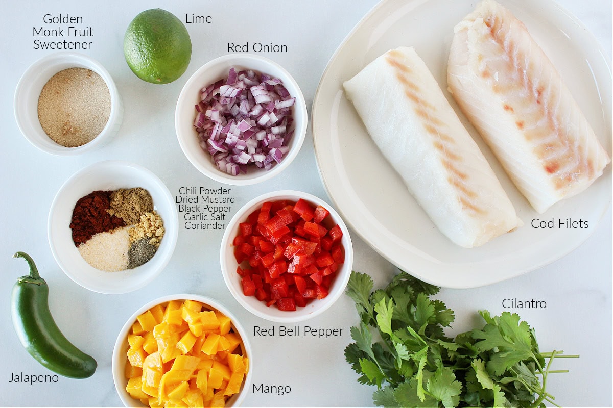 Labeled ingredients for blackened cod with mango salsa on a white marble countertop.