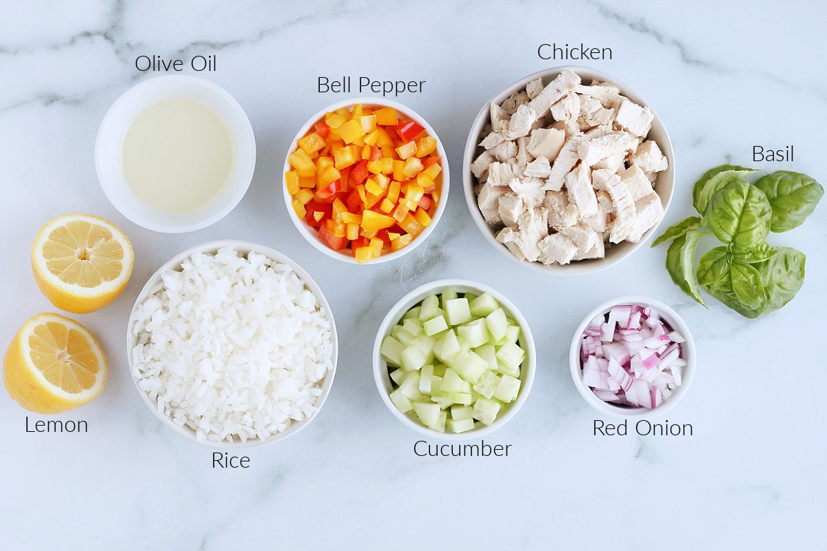 Labeled ingredients for chicken and rice salad with lemon dressing on a white marble countertop.