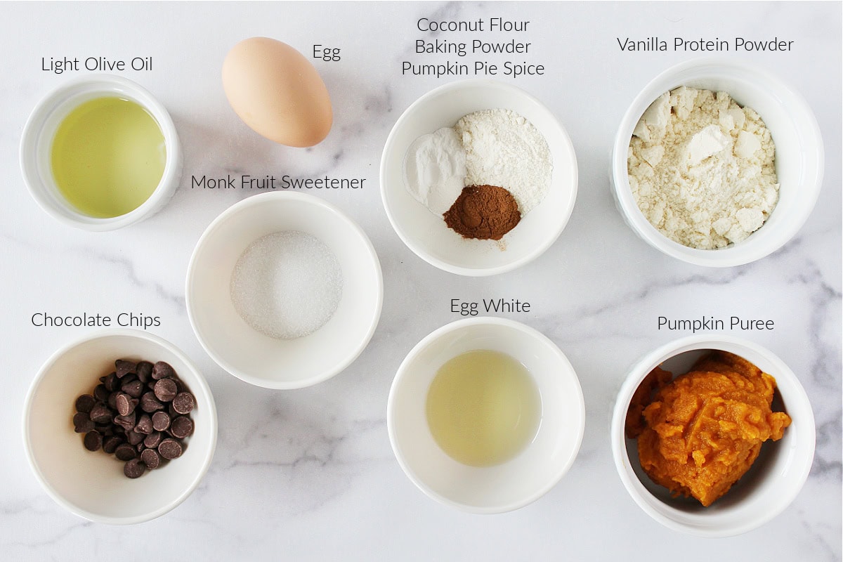 Labeled ingredients for protein pumpkin cake on a white marble countertop.