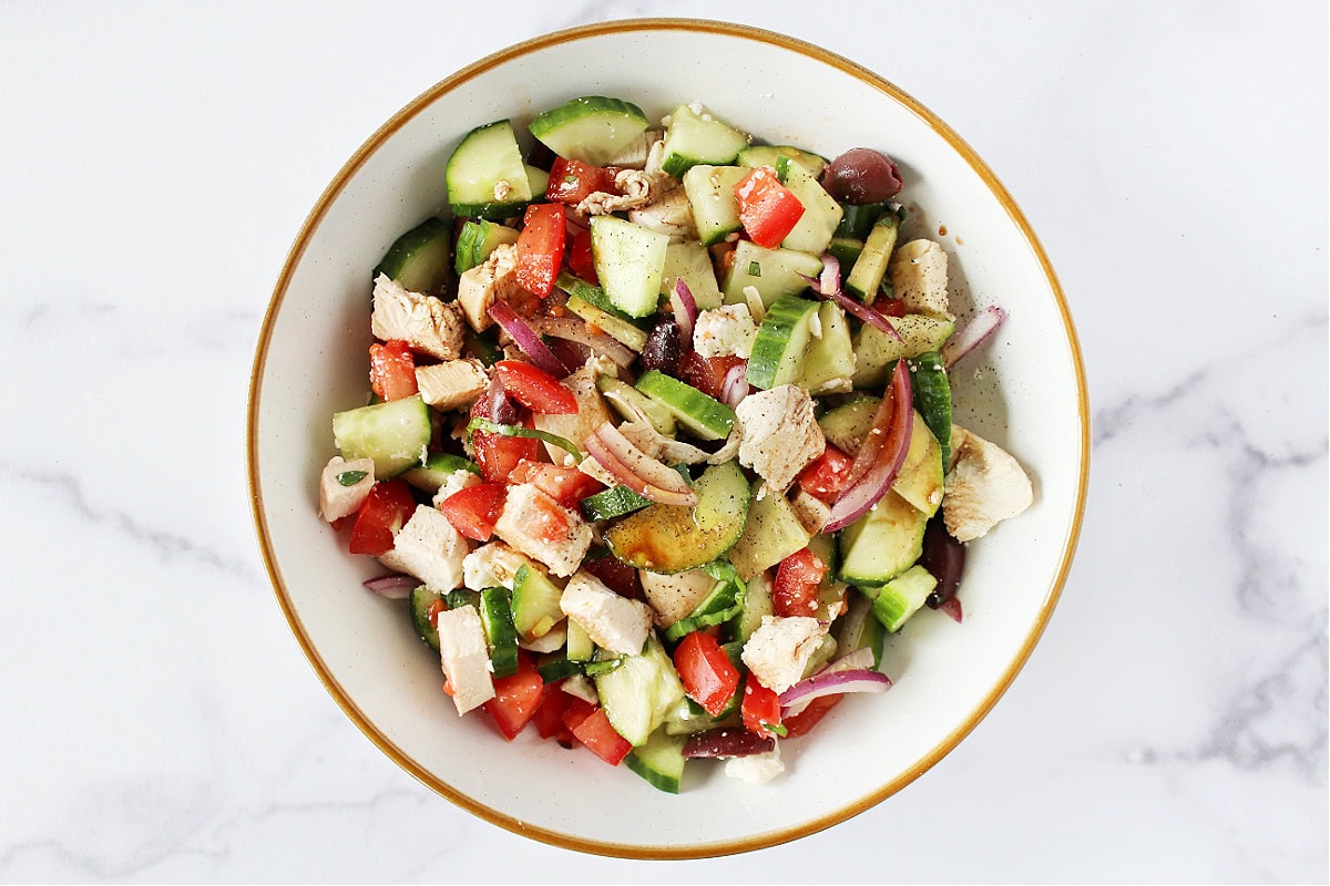 Grilled chicken, cucumbers, olives, onion and feta with dressing in a bowl.