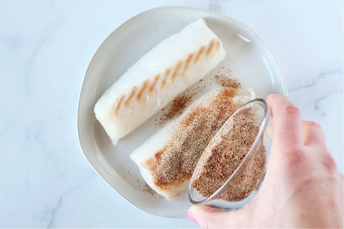 Pouring a homemade seasoning rub on two cod filets.