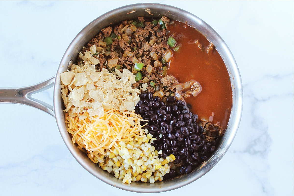 Red enchilada sauce, black beans, ground beef, cheese and tortilla chips in a saute pan.