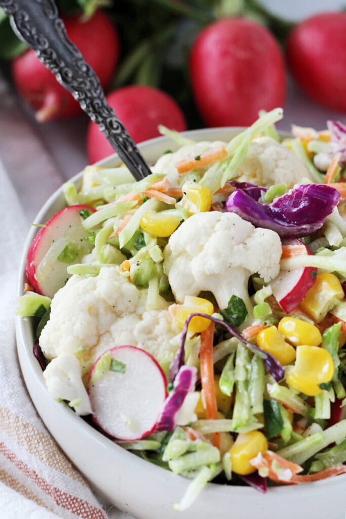 Fresh vegetables coated in a basil mayo dressing in a white bowl with a spoon.