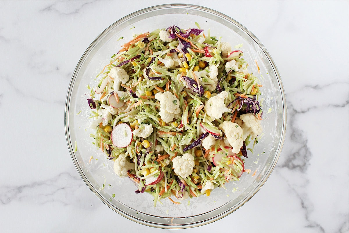 A freshly mixed salad with broccoli slaw, cauliflower and corn in a mayo dressing.