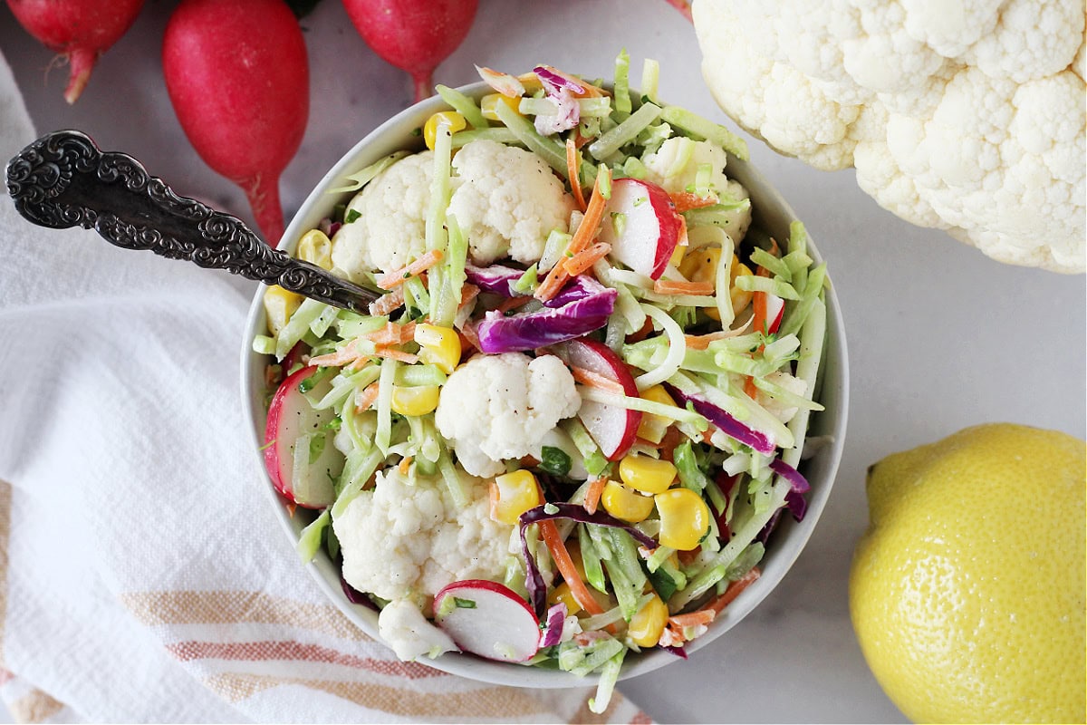 A vintage spoon in a bowl of cauliflower and broccoli slaw salad with corn.