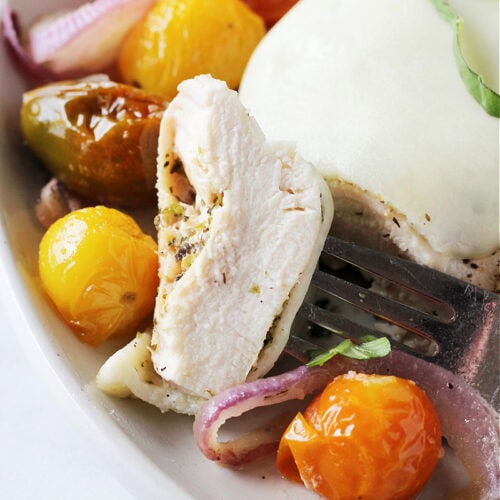 Chicken breast on a fork surrounded by roasted tomatoes and red onion.