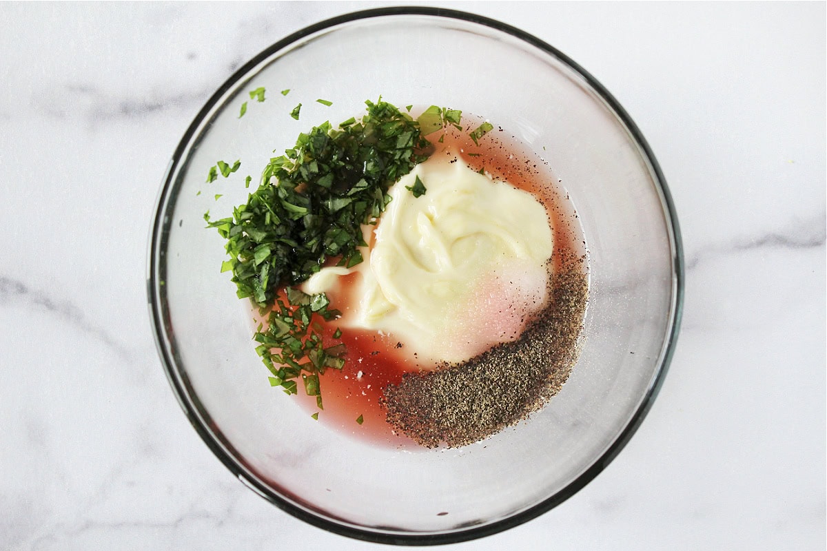 Chopped basil, black pepper, salt, red wine vinegar and mayo in a glass bowl.