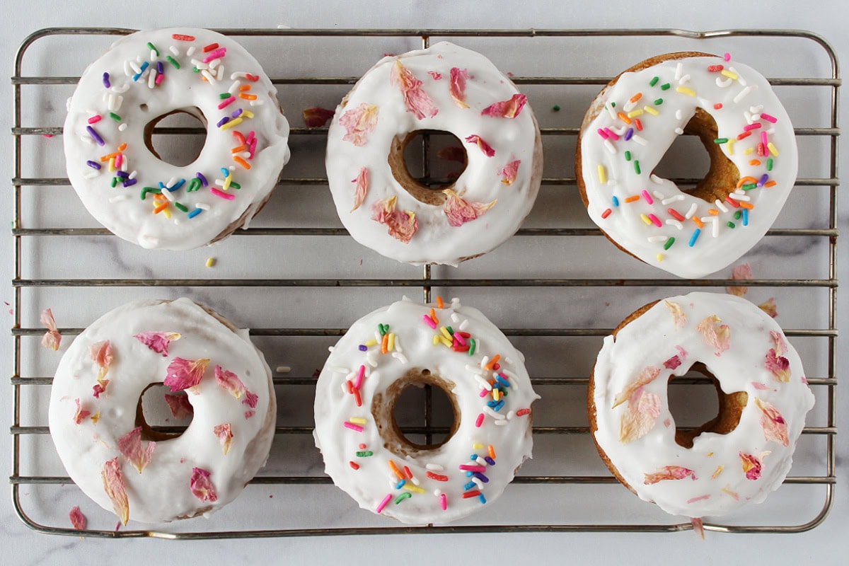 Six donuts topped with vanilla glaze and either colorful sprinkles or dried rose petals.