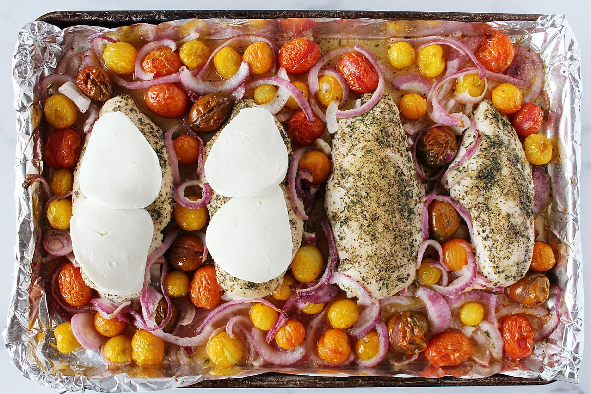 Fresh mozzarellas slices placed on two baked chicken breasts.