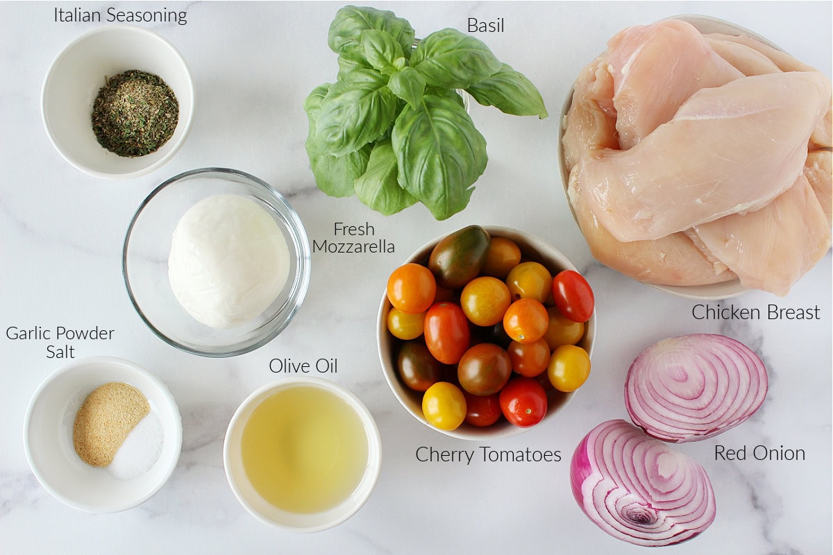 Labeled ingredients for bruschetta chicken sheet pan dinner on a white marble countertop.