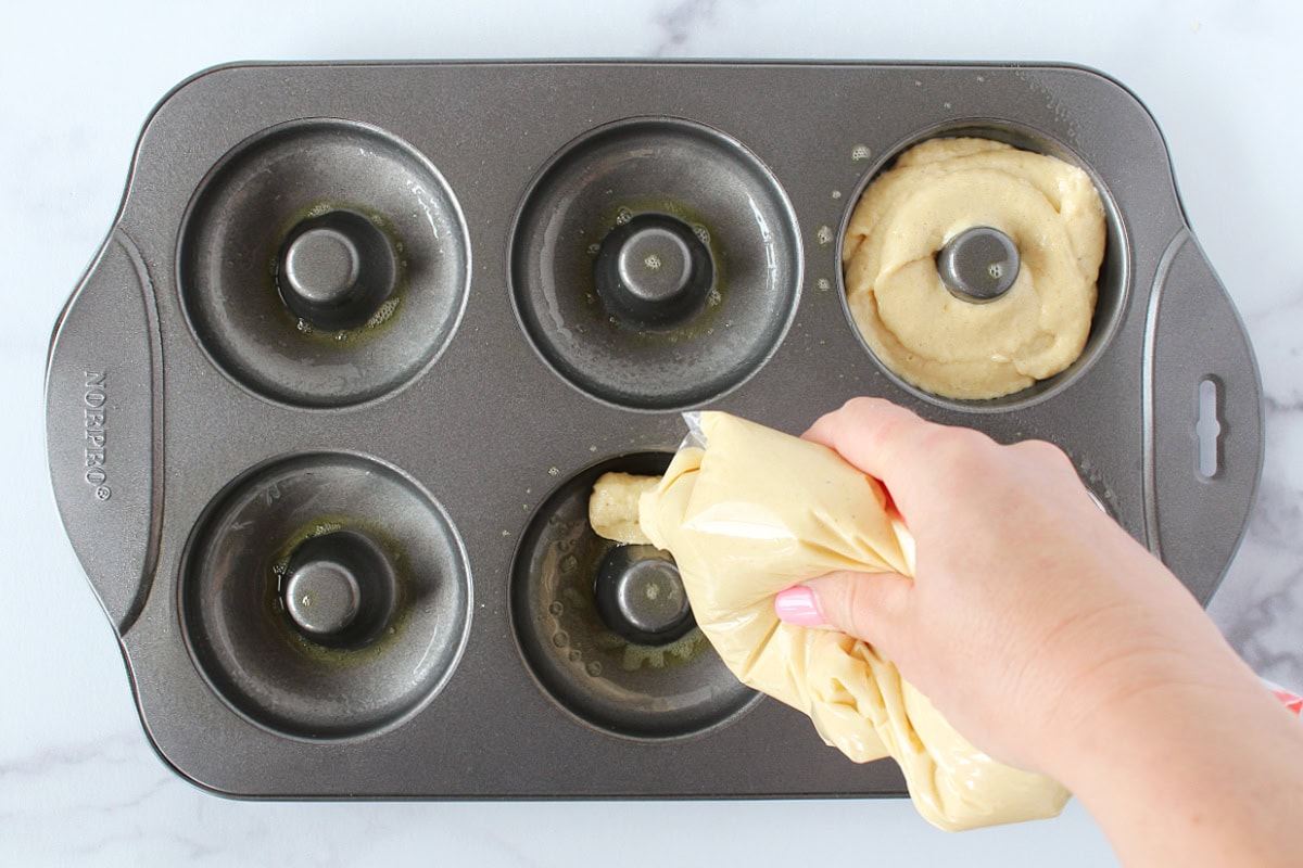 A woman squeezing donut batter from a quart-sized bag into donut pan wells.