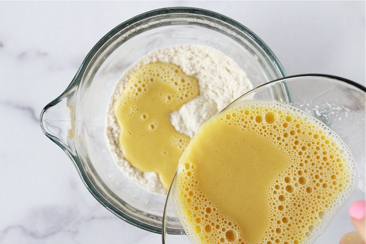 Pouring wet ingredients into dry ingredients in glass bowls.