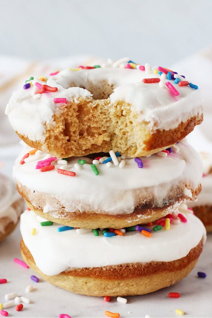 Three donuts topped with a vanilla glaze and colorful sprinkles stacked on top of each other.