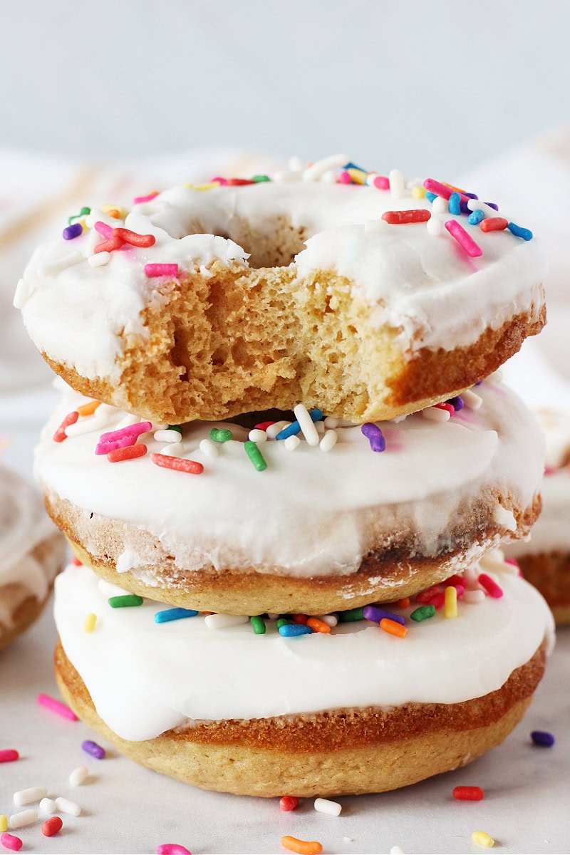 Three donuts topped with a vanilla glaze and colorful sprinkles stacked on top of each other.