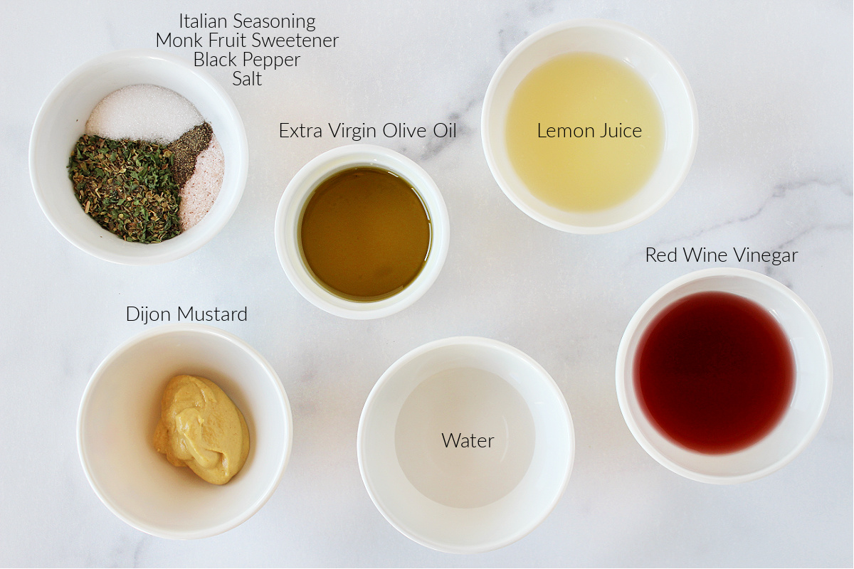 Italian dressing ingredients labeled and in bowls on a white marble countertop.