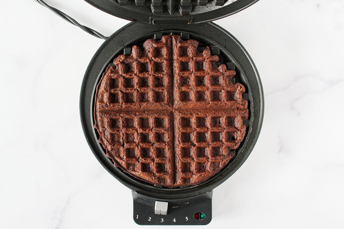 A cooked chocolate waffle in a round waffle maker.