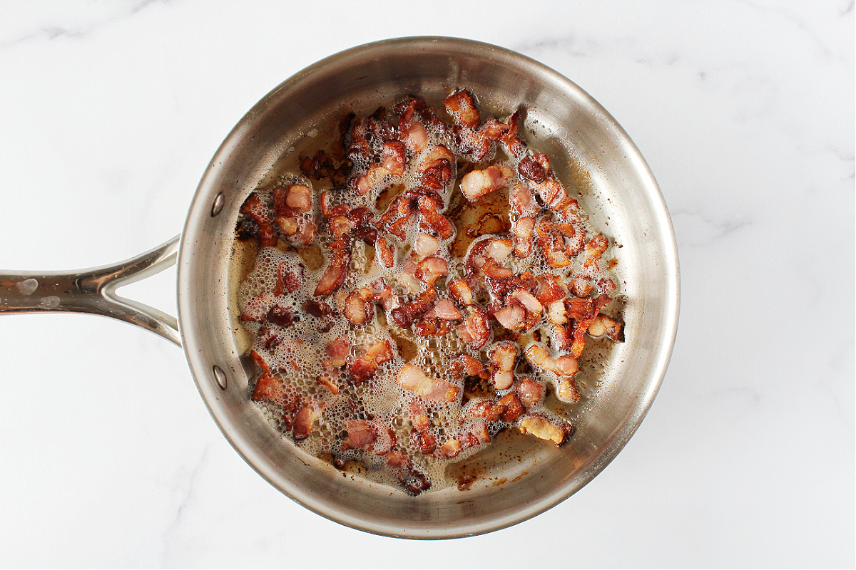 Cooked diced bacon in bacon fat in a stainless steel sauté pan.
