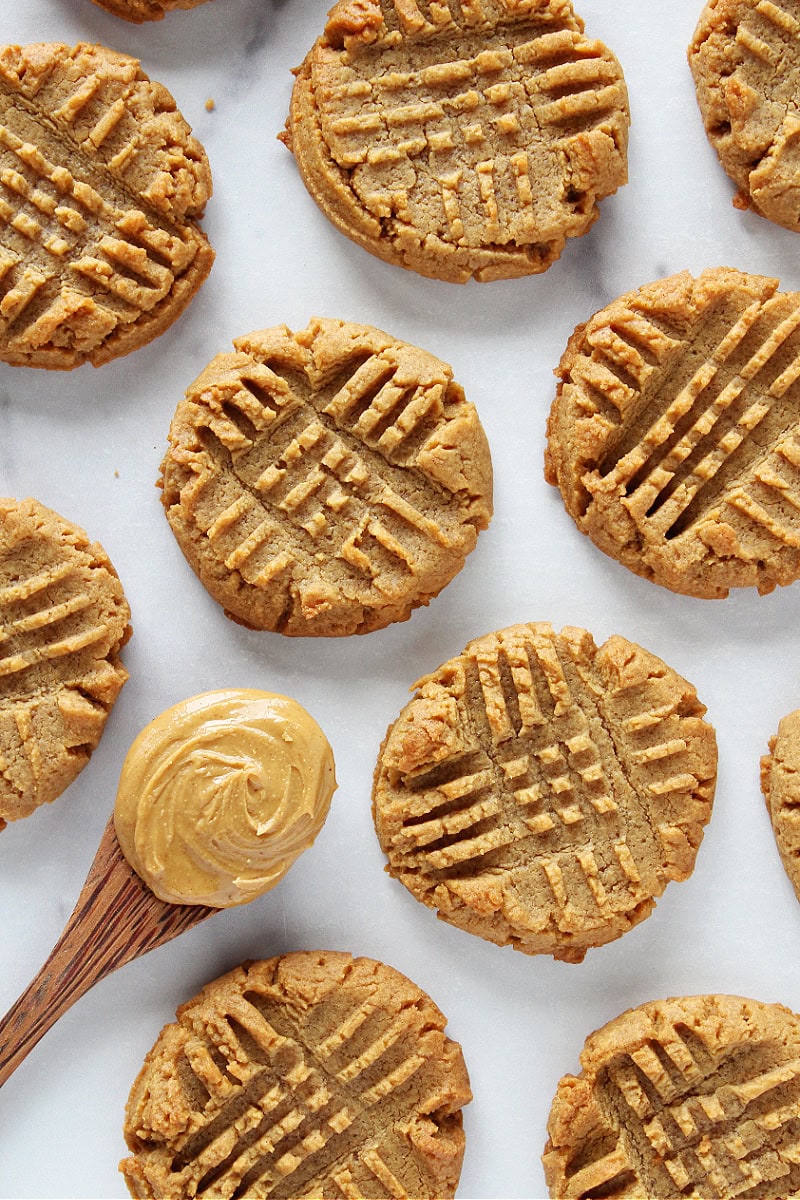 Baked peanut butter cookies on a white countertop with a spoon of peanut butter.