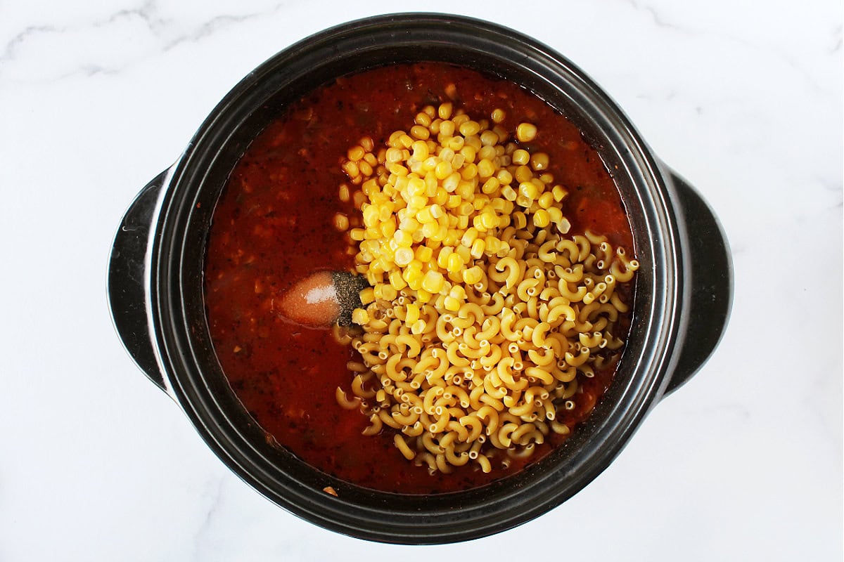 Elbow macaroni, corn, salt and black pepper on top of a tomato veggie mixture.
