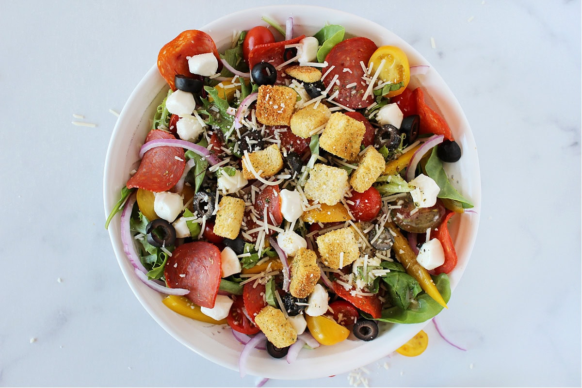Croutons, shredded Parmesan cheese and Italian dressing on pizza salad in a white bowl.