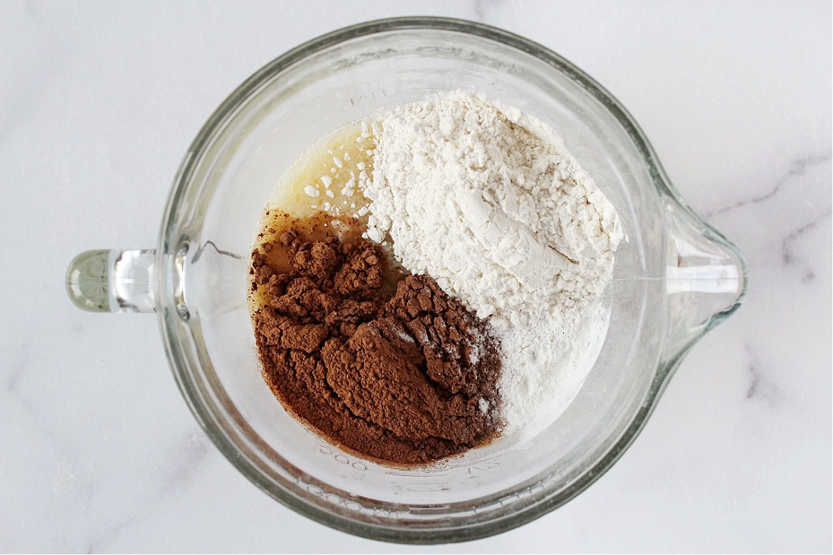 Gluten free flour, cocoa powder, and leavener on top of wet ingredients in a bowl.