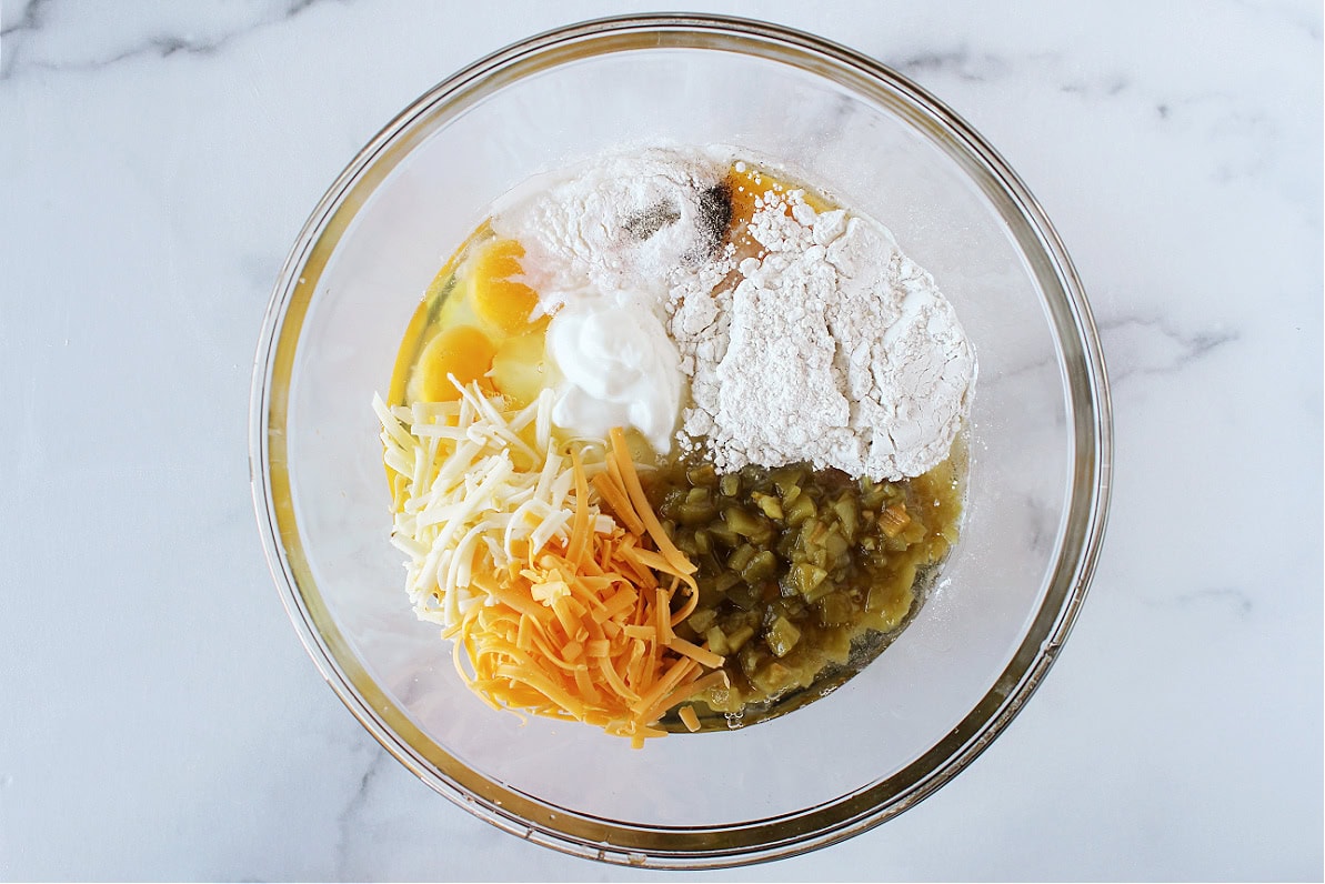 Eggs, plain Greek yogurt, flour, shredded cheese, and diced green chiles in a mixing bowl.
