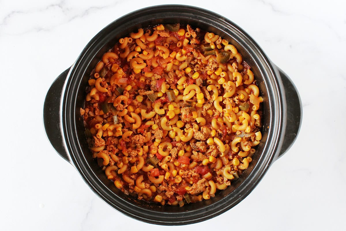 Ground meat, veggies, and elbow macaroni in goulash in a black pot.