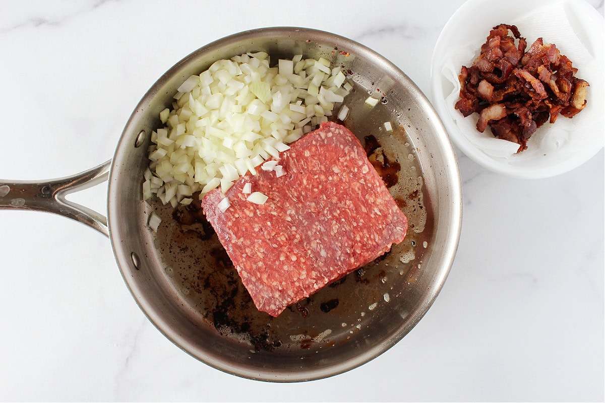 Ground beef and diced onion in a pan with cooked bacon in a bowl.