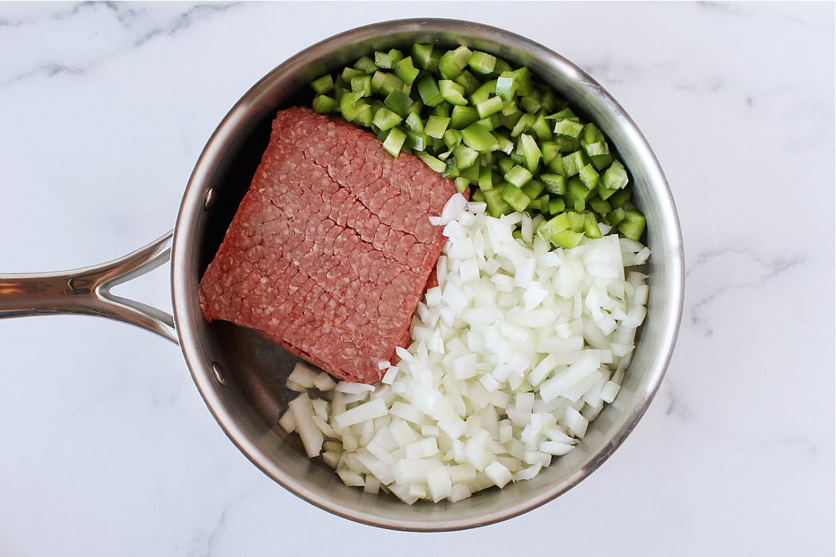 Raw ground beef, diced bell pepper, and onion in a saucepan.