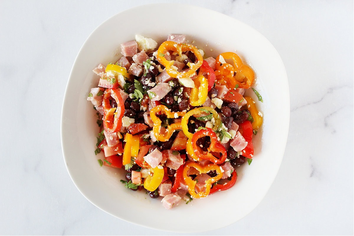 Mini bell pepper rings, veggies, black beans, and ham mixed in a bowl.