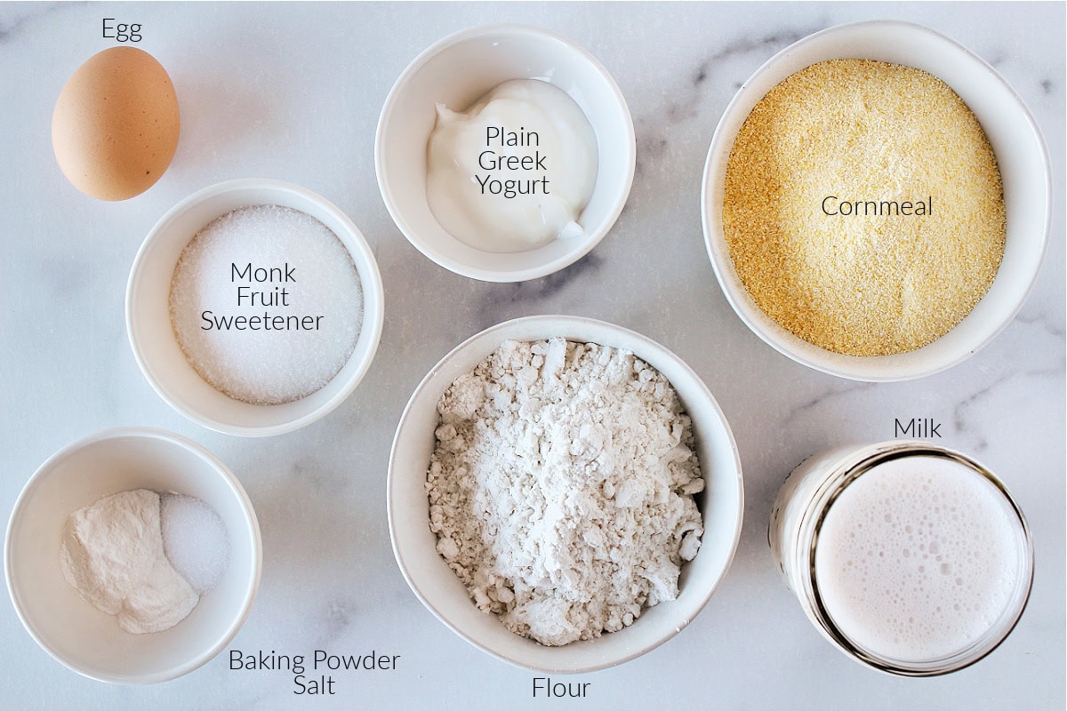 Labeled ingredients for cornbread on a white marble countertop.