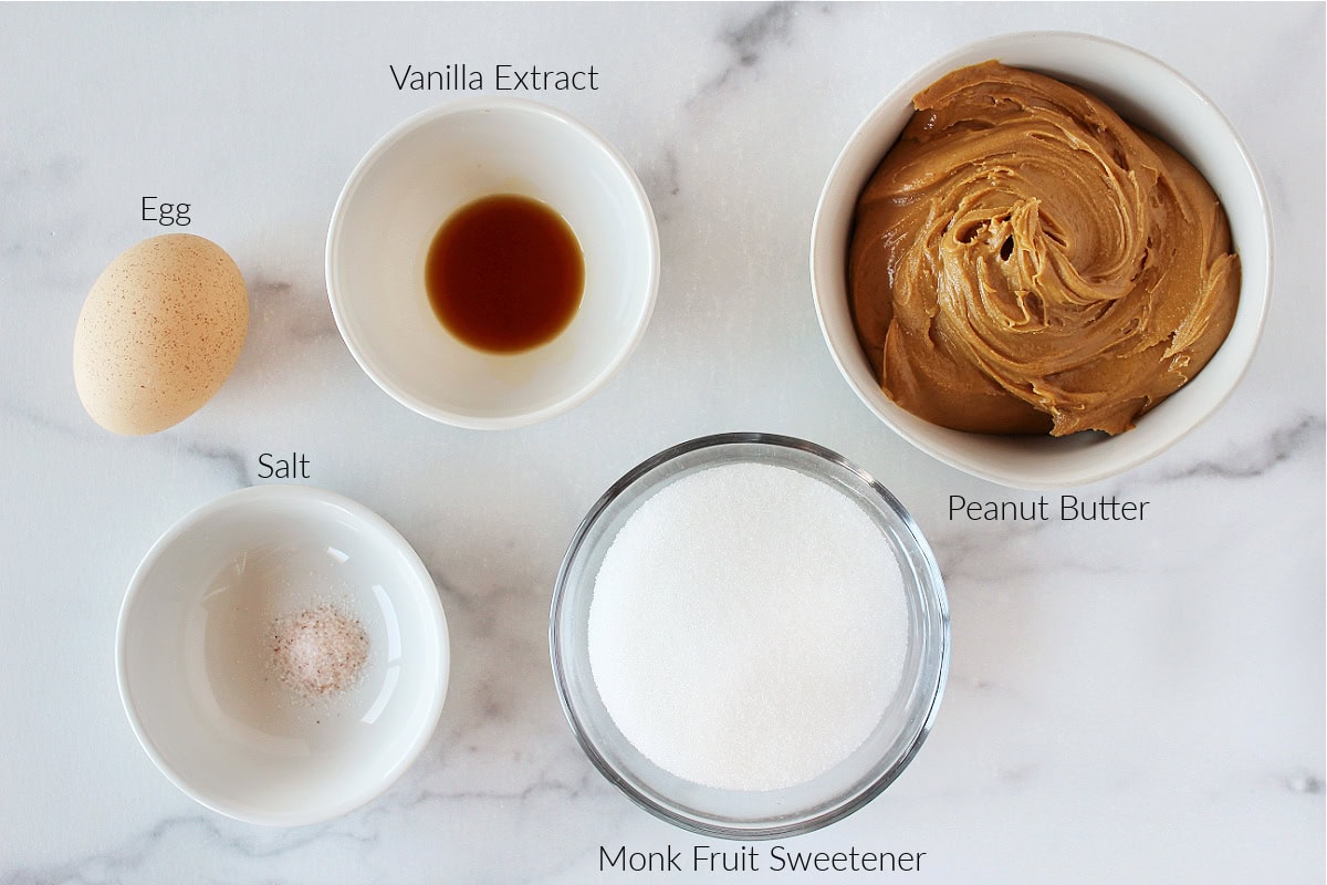 Labeled ingredients for flourless peanut butter cookies on a white marble countertop.