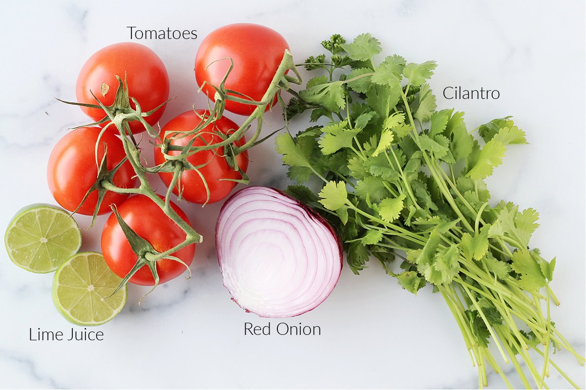 Labeled ingredients for homemade pico de gallo on a white marble countertop.