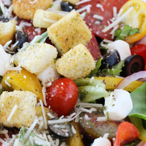 Croutons, mozzarella pearls, croutons, and fresh veggies in a bowl.