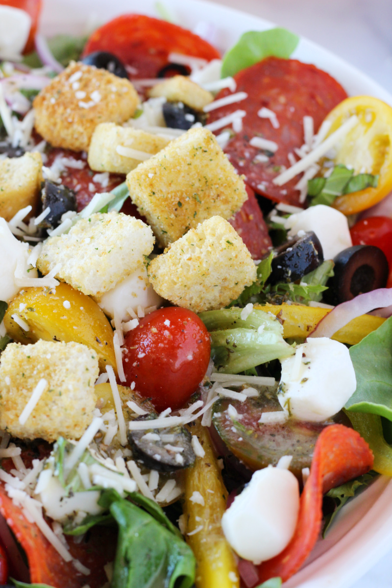 Croutons, mozzarella pearls, croutons, and fresh veggies in a bowl.
