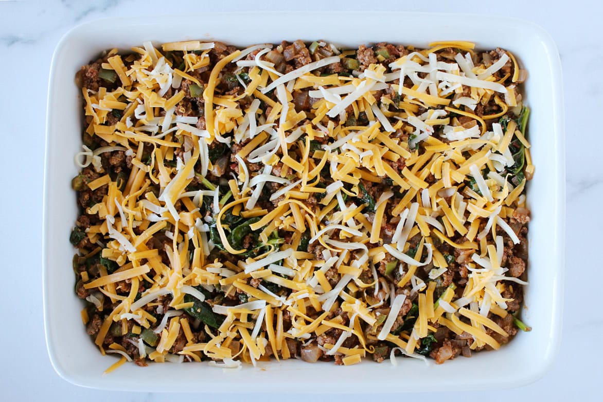 Shredded cheese on top of browned ground beef and sauteed vegetables.