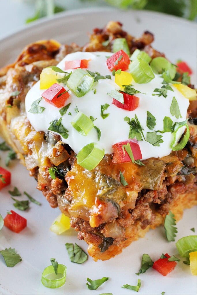 A piece of Mexican cornbread casserole topped with sour cream, cilantro and peppers.
