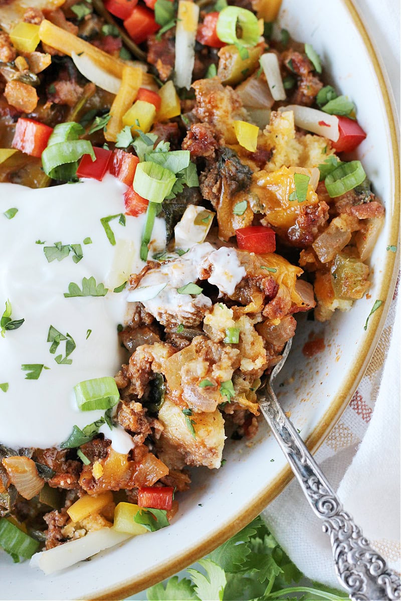 A spoon in a bowl of cornbread casserole with Greek yogurt on top.